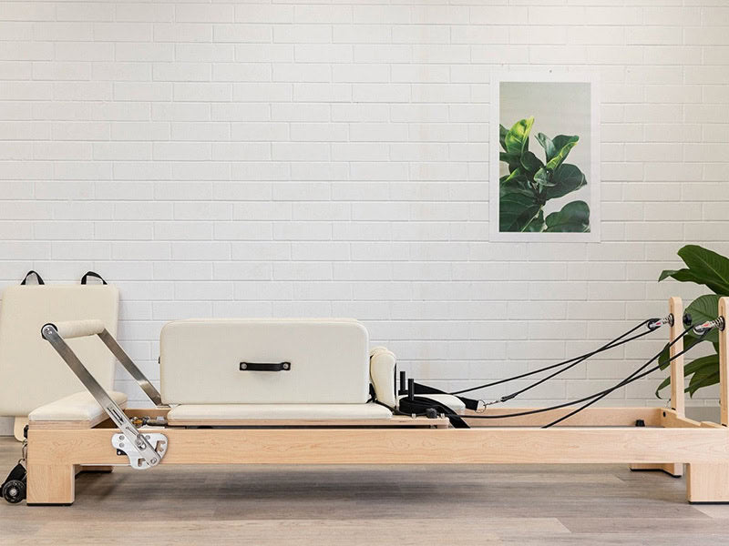 Red Pilates wood reformer machine in a room with a white brick wall and a plant.
