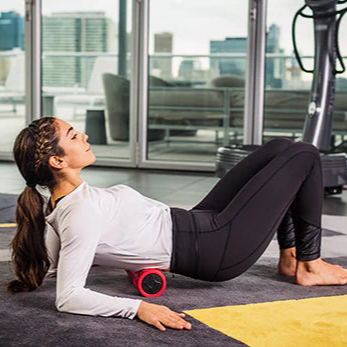 Woman using a red Power Plate roller on a mat with a cityscape view in the background